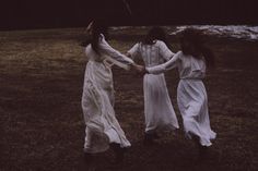 three women in white dresses holding hands and walking through a field with snow on the ground