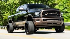 a black ram truck driving down the road with big tires on it's wheels