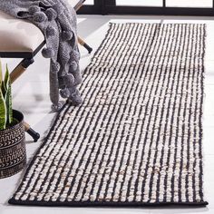 a black and white striped rug on the floor next to a chair with a potted plant