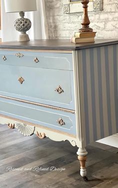 an old dresser painted in blue and white with gold trimmings, sits on a hard wood floor next to a lamp