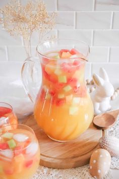 a pitcher filled with fruit sitting on top of a wooden tray next to two glasses