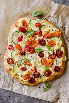 an uncooked pizza with tomatoes, zucchini and other toppings on top