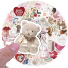 a hand holding up a white teddy bear sticker in front of a circular background