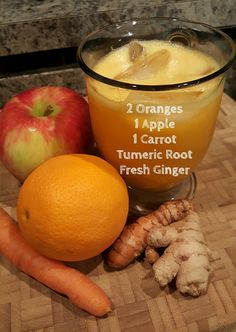 oranges, carrots, and an apple sit on a cutting board next to some juice