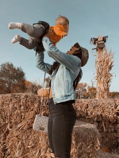 a woman holding a baby in her arms while standing next to a scarecrow and camera