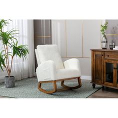 a white rocking chair next to a potted plant on a rug in front of a window