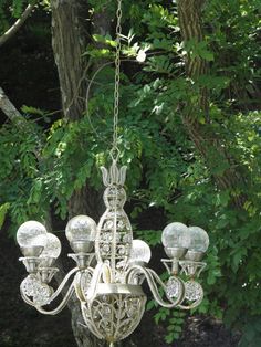 a chandelier hanging from a chain in front of some green leaves and trees