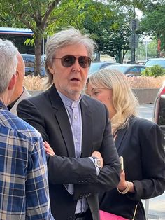 a man in a suit and sunglasses talking to two other people on the side walk