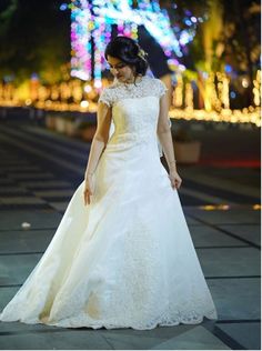 a woman in a white wedding dress walking down the street at night with lights behind her