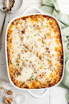 a casserole dish with meat and cheese in it on a white table next to garlic