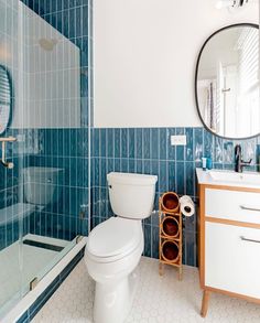 a white toilet sitting next to a walk in shower under a bathroom mirror on top of a wooden cabinet