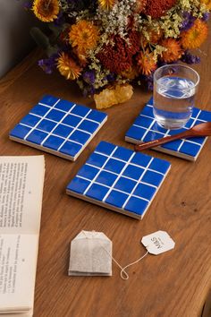 a wooden table topped with blue tiles next to a vase filled with flowers and an open book