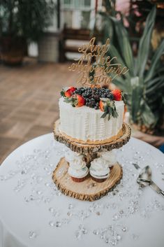 a wedding cake with berries on top sits on a table