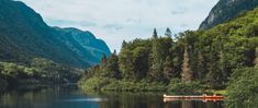 a boat floating on top of a lake surrounded by trees and mountains in the background