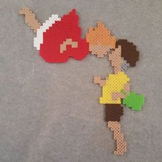 two pieces of perler bead art depicting children playing with each other on a gray surface