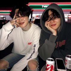 two young men sitting next to each other in front of a neon lit building at night