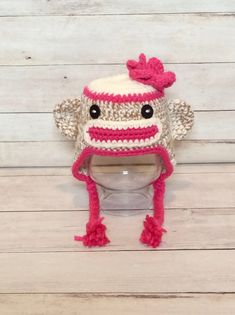 a crocheted sock monkey hat sitting on top of a toilet bowl with pink pom poms