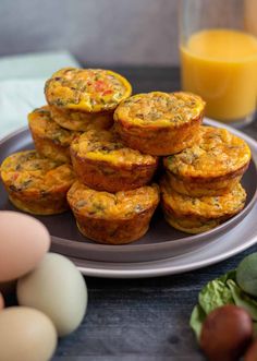 several muffins on a plate next to eggs and orange juice in the background