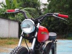 a red and black motorcycle parked on top of a cement ground next to trees in the background