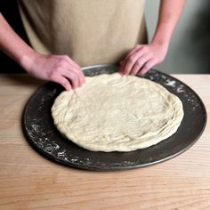 a person kneading dough on top of a metal pan in front of a wooden table