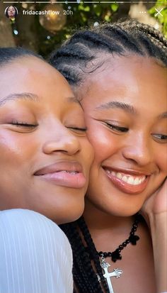 two girls are smiling and hugging each other with their heads close to one another, both wearing necklaces