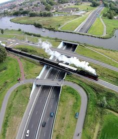 an aerial view of a train traveling down the tracks near a river and road intersection