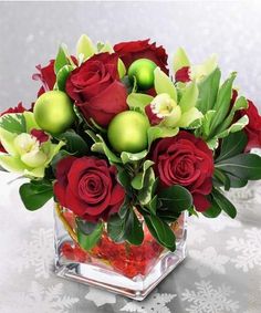 a glass vase filled with red roses and green balls on top of a white table cloth