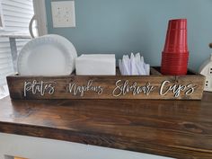 a wooden sign sitting on top of a counter next to plates and napkins in front of a window