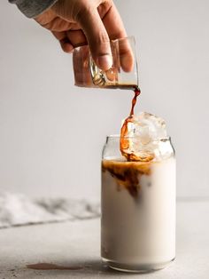 someone is pouring something into a glass with ice and caramel in it on the table