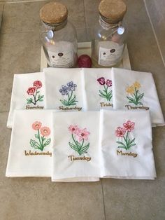 four tea towels with embroidered flowers on them sitting on the floor next to two bottles