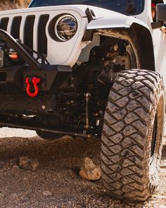 the front end of a white jeep parked on top of a dirt field next to rocks