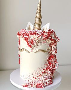 a white and red cake with a unicorn face on it's side, topped with sprinkles