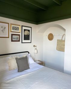 a bed with white sheets, pillows and pictures on the wall