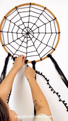 a woman is making a dream catcher out of string and wood beads on the wall