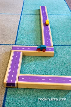 a toy truck driving down a road made out of wooden blocks on top of blue carpet