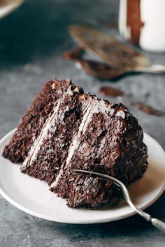 a piece of chocolate cake on a white plate with a fork in front of it