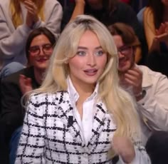 a woman with long blonde hair is sitting in front of a crowd and giving a thumbs up