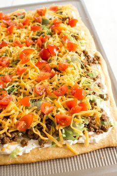 an uncooked pizza topped with cheese, tomatoes and other toppings on a baking sheet