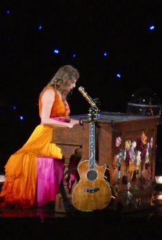 a woman in an orange dress is playing the guitar