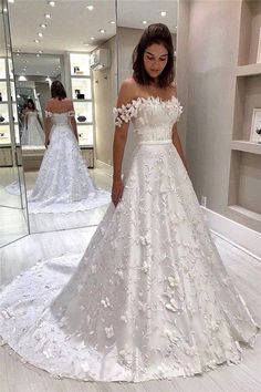 a woman standing in front of a mirror wearing a wedding dress with flowers on it