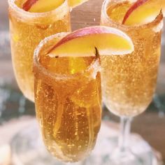 three glasses filled with apple cider on top of a wooden table next to an orange slice