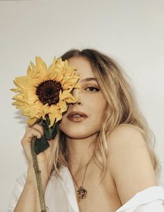 a woman holding a sunflower in front of her face and looking at the camera