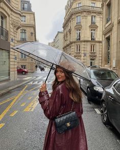 a woman holding an umbrella while standing on the side of a road next to parked cars