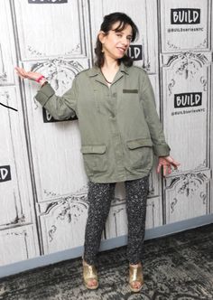 a woman standing in front of a white wall with an open hand sign on it