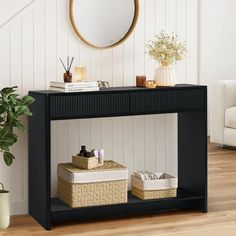 a black console table with two baskets under it and a round mirror on the wall