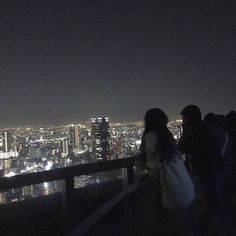 people standing on top of a building looking at the city lights in the night sky