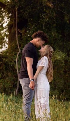 a man and woman are standing in the grass kissing each other with trees in the background