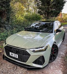 a light green car parked on the side of a road next to trees and bushes