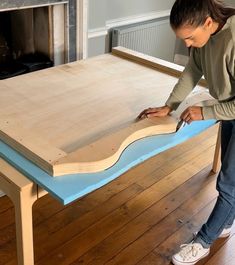 a woman is working on a table with blue paint and plywood trimmings