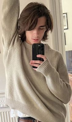 a young man taking a selfie with his cell phone while wearing jeans and a sweater